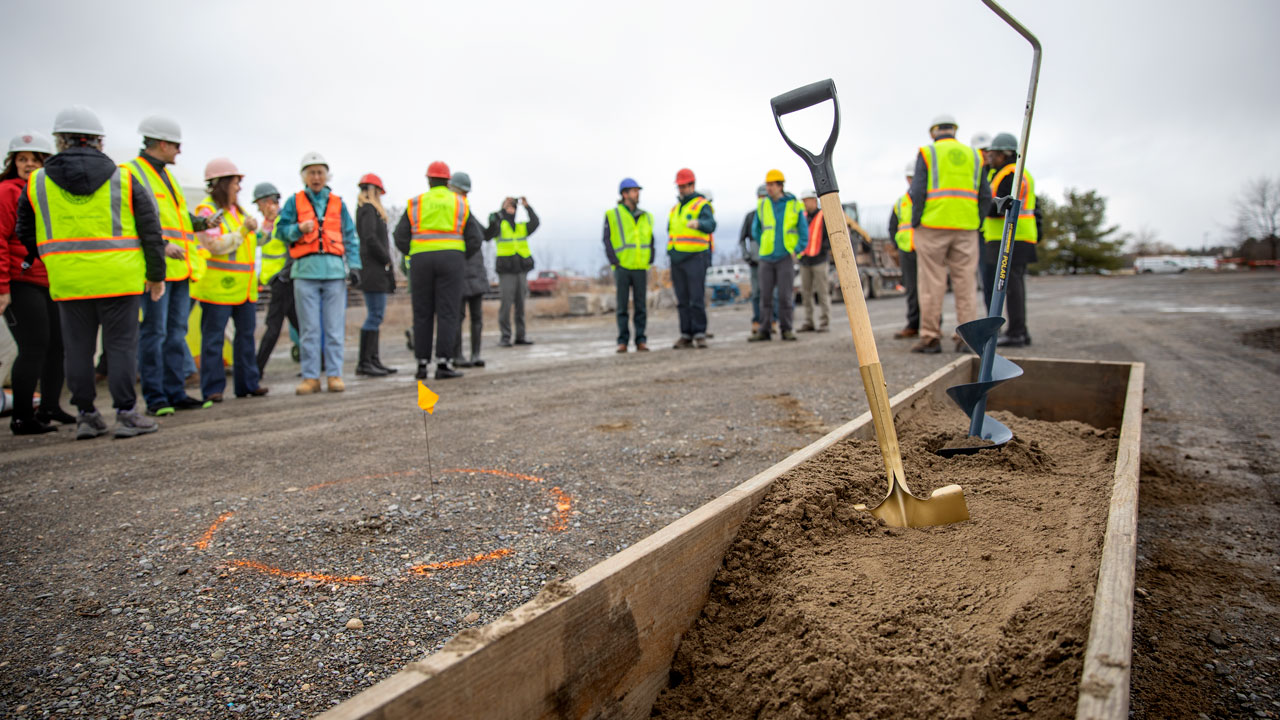 While members of the project team and others gather nearby, a golden shovel and auger rest in the earth during the groundbreaking ceremony for the Cornell University Borehole Observatory (CUBO).